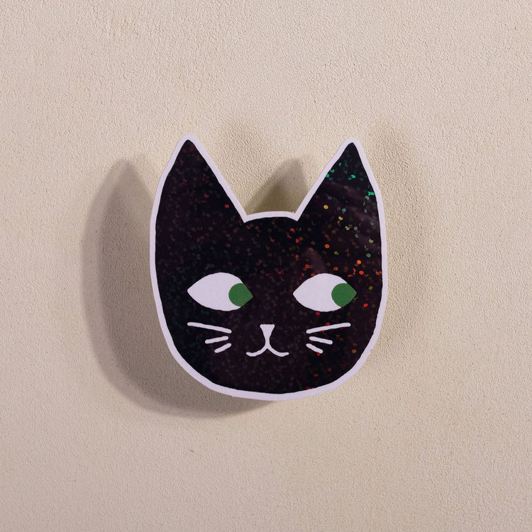 Glitter Cat Head Sticker with a black cat face, green eyes, and sparkly glitter details on a beige background