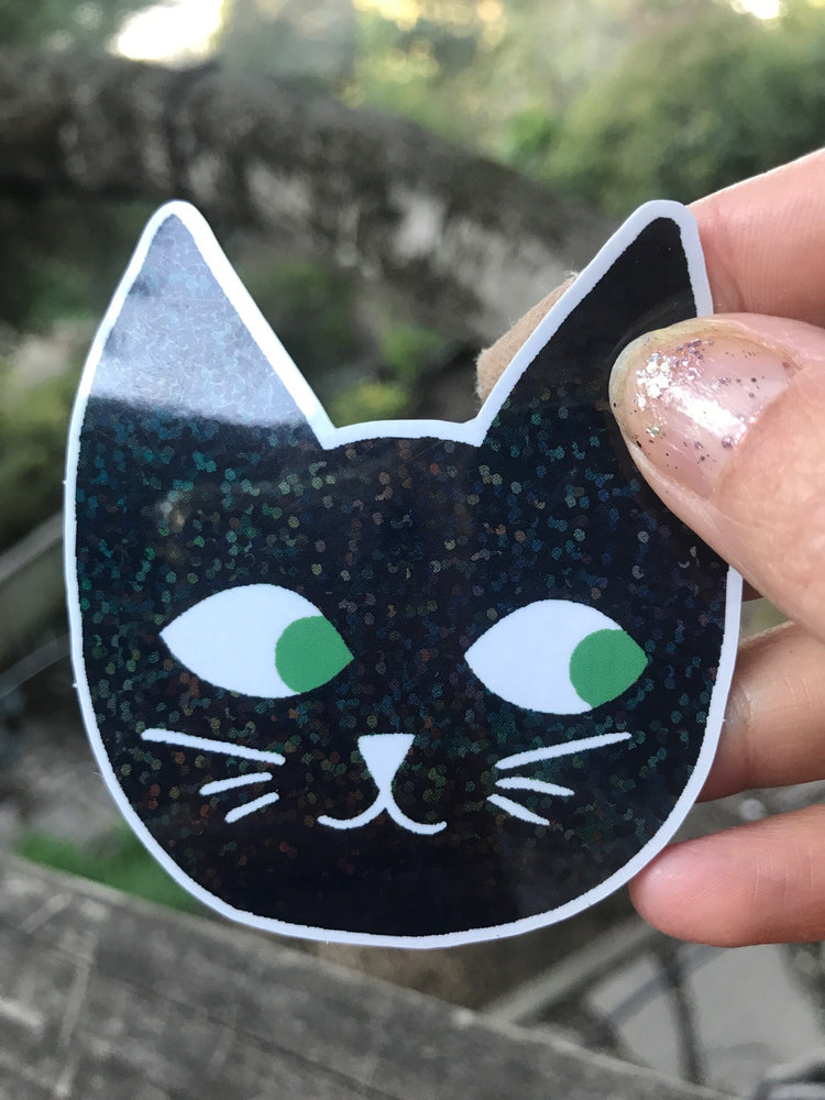 Glitter Cat Head Sticker with black cat face and green eyes sparkly glitter details held outdoors in natural light