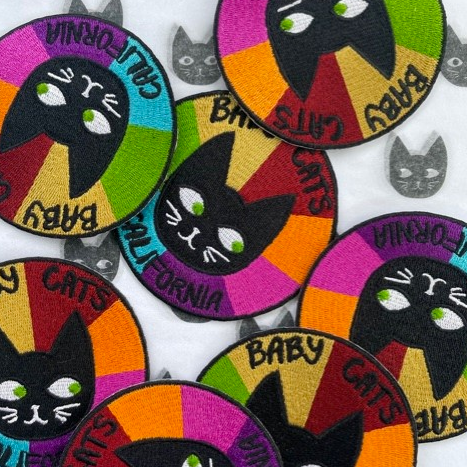 Cat Patch featuring a black cat face with bright rainbow color blocks and playful text around the edge