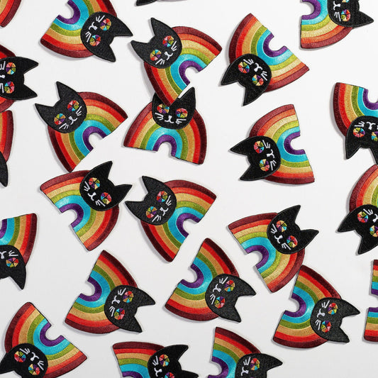 Rainbow Cat Patch with cheerful black cat faces and vibrant rainbow arcs on embroidered fabric accessories scattered on white background